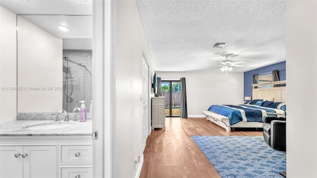 bedroom with baseboards, visible vents, light wood-style flooring, a sink, and a textured ceiling