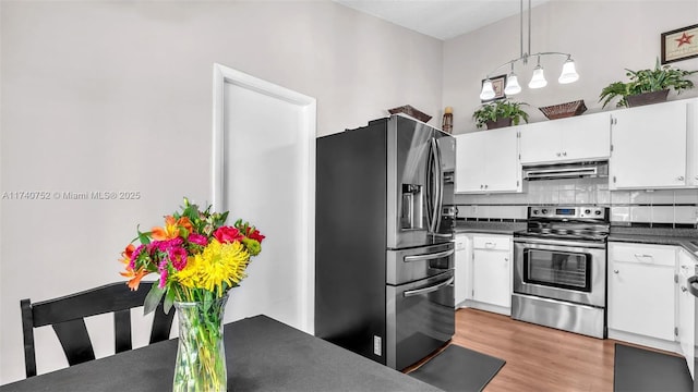 kitchen with under cabinet range hood, stainless steel appliances, dark countertops, and white cabinets