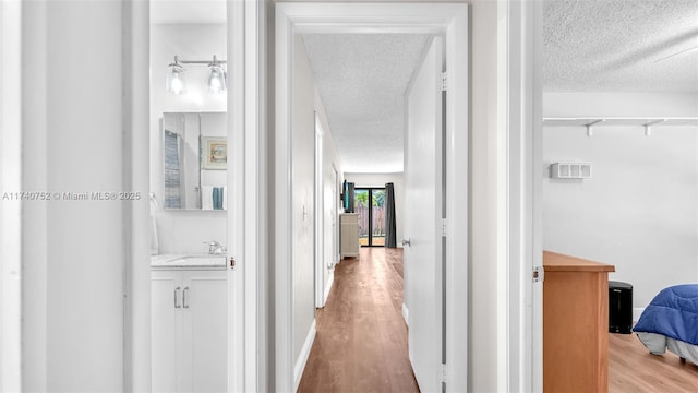 hallway featuring a sink, baseboards, a textured ceiling, and wood finished floors