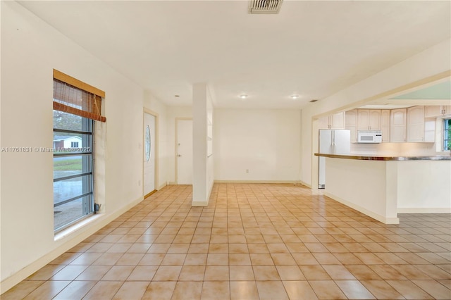 unfurnished living room with light tile patterned floors, visible vents, a healthy amount of sunlight, and baseboards