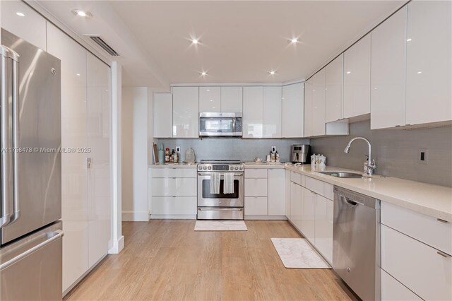 kitchen featuring light wood-type flooring, white cabinets, stainless steel appliances, modern cabinets, and a sink