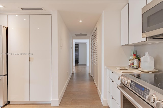 hall featuring light wood-type flooring, visible vents, baseboards, and recessed lighting