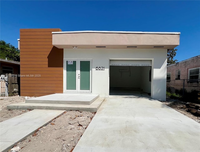 view of front facade featuring fence, concrete driveway, stucco siding, french doors, and a garage