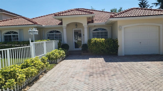 mediterranean / spanish-style home with stucco siding, an attached garage, decorative driveway, and fence