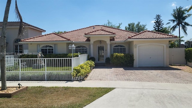 mediterranean / spanish house with decorative driveway, a fenced front yard, an attached garage, and stucco siding