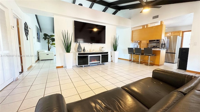 living area featuring visible vents, vaulted ceiling with beams, ceiling fan, light tile patterned flooring, and a glass covered fireplace