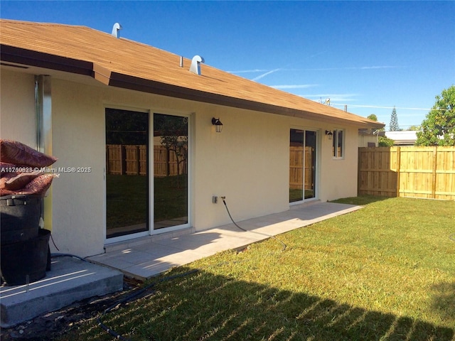 back of property with stucco siding, a lawn, and fence