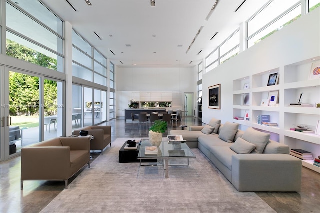 living room with a wall of windows, a high ceiling, built in shelves, and concrete floors