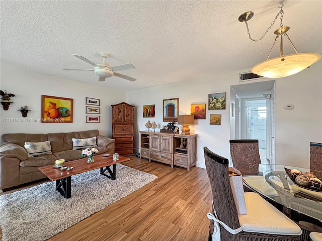 living room with a ceiling fan, visible vents, light wood-type flooring, and a textured ceiling