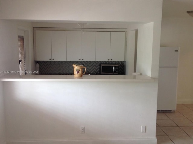 kitchen with stainless steel microwave, light countertops, light tile patterned floors, freestanding refrigerator, and white cabinetry