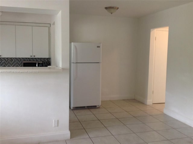 kitchen with stainless steel microwave, freestanding refrigerator, white cabinets, light countertops, and light tile patterned floors