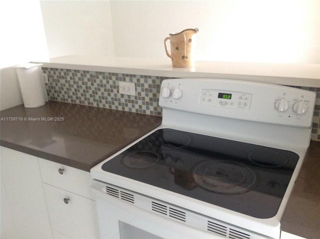 kitchen featuring dark countertops, electric range, white cabinetry, and decorative backsplash