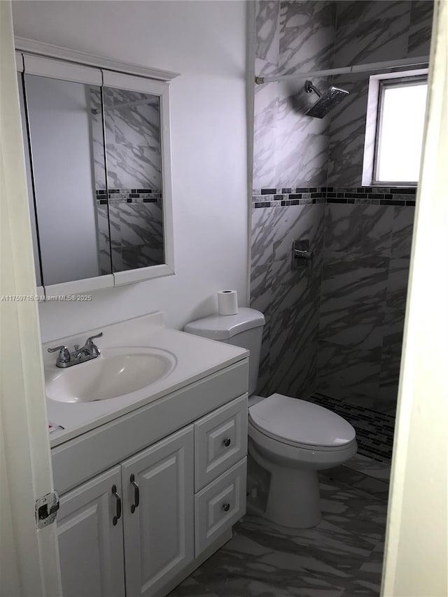 full bath with marble finish floor, tiled shower, vanity, and toilet