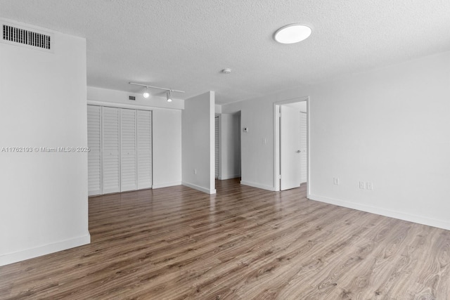 spare room with visible vents, a textured ceiling, baseboards, and wood finished floors