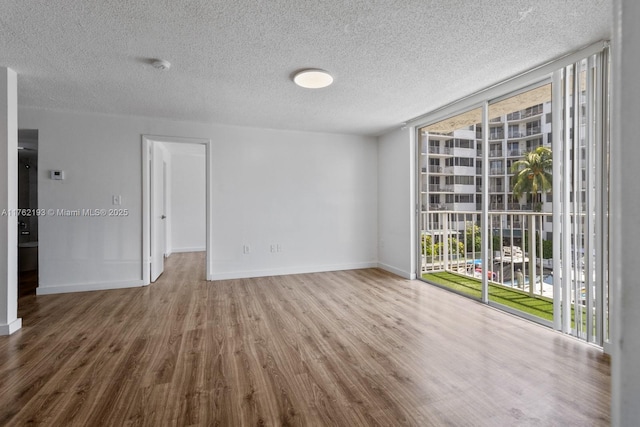 spare room featuring floor to ceiling windows, a textured ceiling, baseboards, and wood finished floors