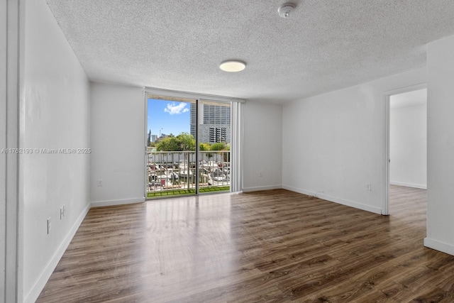 unfurnished room featuring a textured ceiling, wood finished floors, baseboards, and expansive windows