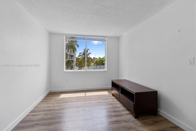 spare room featuring a textured ceiling, baseboards, and wood finished floors