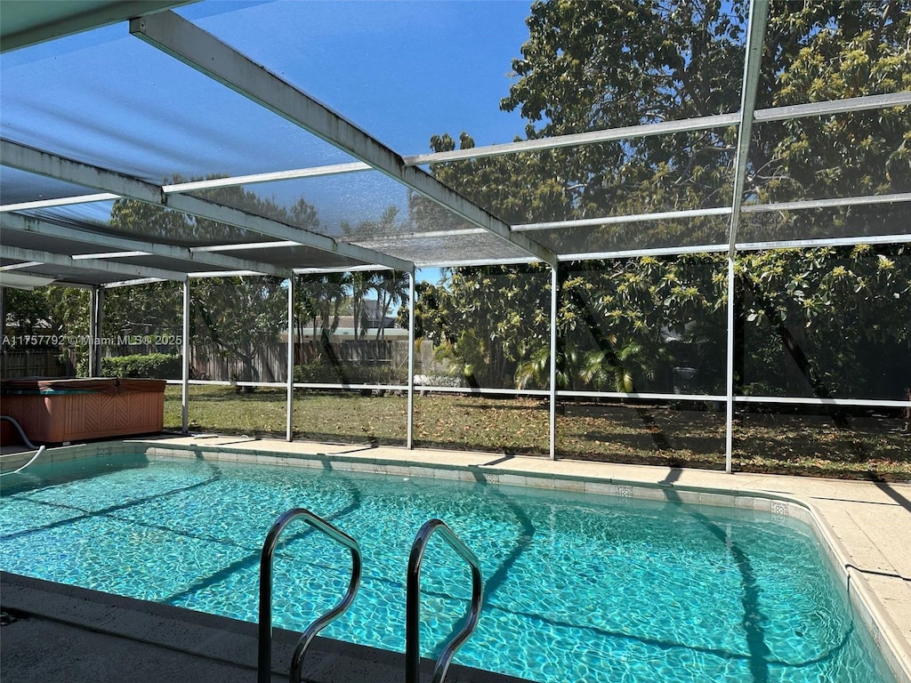 outdoor pool with a patio area, glass enclosure, and a hot tub