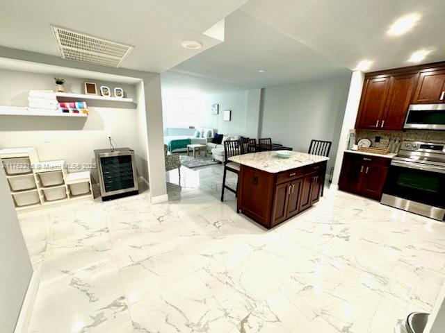 kitchen featuring visible vents, marble finish floor, a kitchen island, appliances with stainless steel finishes, and decorative backsplash