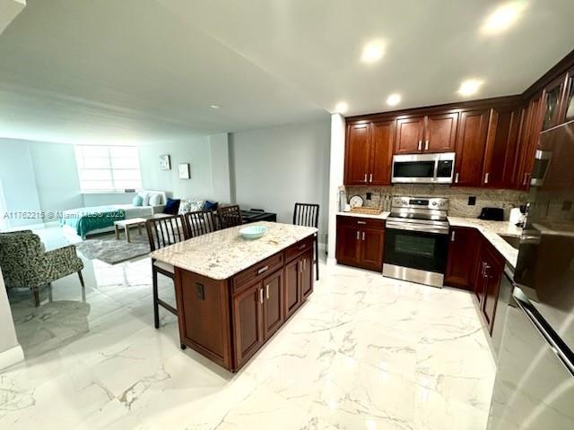 kitchen with decorative backsplash, marble finish floor, appliances with stainless steel finishes, and a kitchen bar