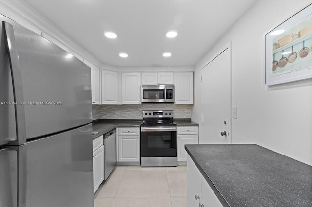 kitchen featuring dark countertops, tasteful backsplash, light tile patterned floors, appliances with stainless steel finishes, and white cabinetry