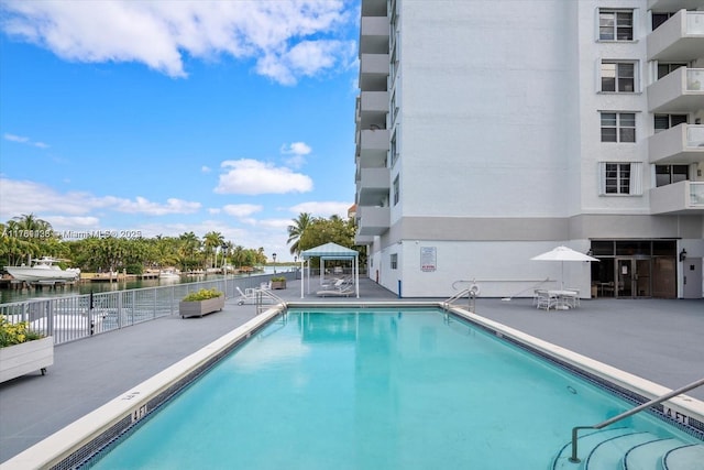 community pool with a gazebo, a water view, and a patio