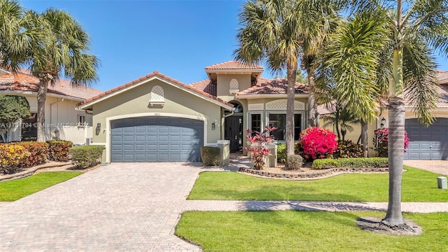 mediterranean / spanish home featuring stucco siding, a front lawn, a tile roof, decorative driveway, and an attached garage