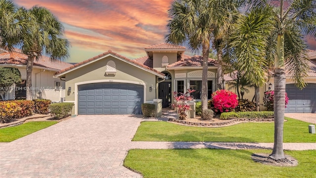 mediterranean / spanish home with stucco siding, decorative driveway, a front yard, an attached garage, and a tiled roof