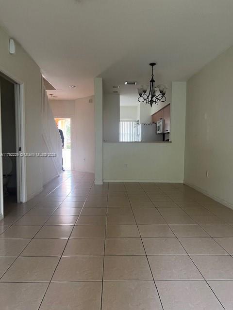 spare room featuring light tile patterned flooring, baseboards, and an inviting chandelier