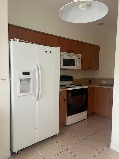 kitchen with light tile patterned floors, brown cabinets, white appliances, and light countertops