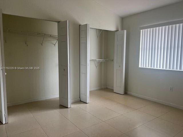 unfurnished bedroom featuring light tile patterned flooring, baseboards, and multiple closets