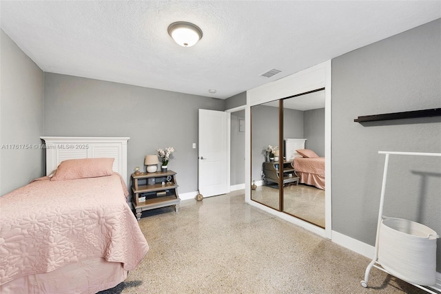 bedroom with a textured ceiling, speckled floor, baseboards, visible vents, and a closet
