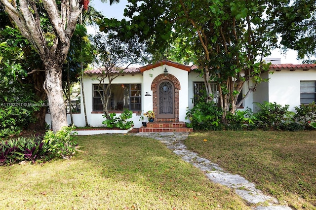 mediterranean / spanish house featuring stucco siding, a tiled roof, and a front lawn