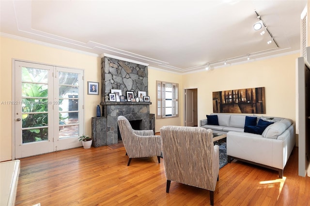 living room featuring a stone fireplace, plenty of natural light, light wood-type flooring, and ornamental molding