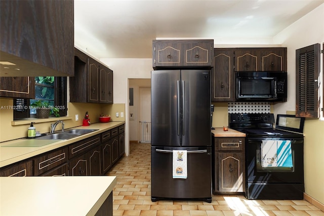 kitchen featuring dark brown cabinets, black appliances, light countertops, and a sink