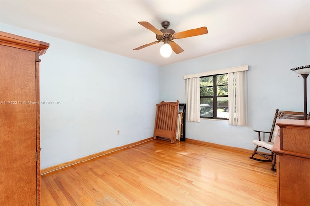 living area featuring baseboards, light wood-style floors, and a ceiling fan