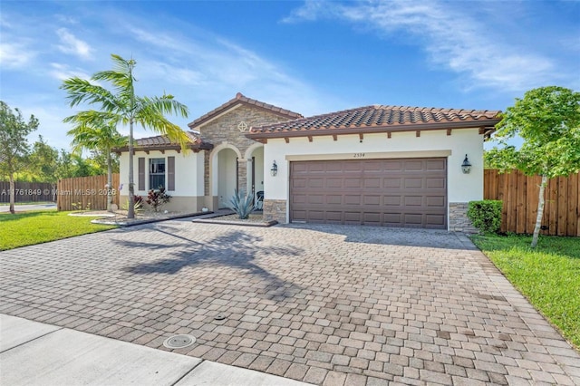 mediterranean / spanish house with fence, stucco siding, decorative driveway, a garage, and stone siding