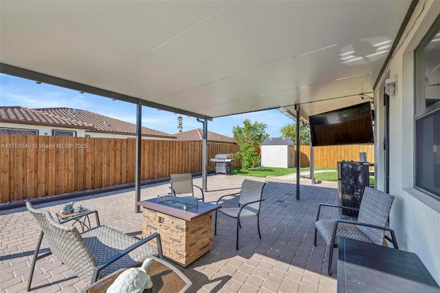 view of patio featuring an outbuilding, a fenced backyard, a storage unit, a fire pit, and grilling area