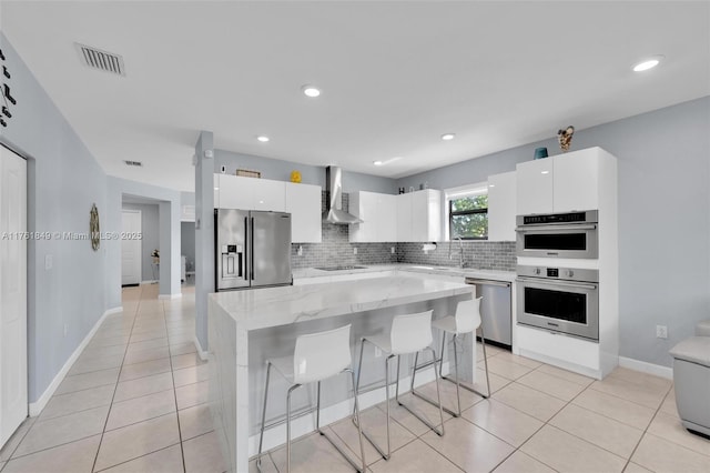 kitchen featuring visible vents, modern cabinets, a breakfast bar, appliances with stainless steel finishes, and wall chimney range hood