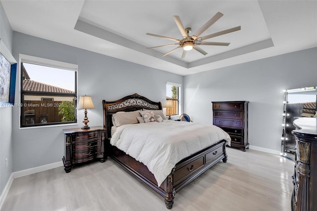 bedroom with a tray ceiling, baseboards, wood finished floors, and a ceiling fan