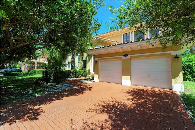 view of front facade with stucco siding, decorative driveway, and a garage