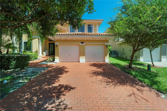 mediterranean / spanish house featuring stucco siding, decorative driveway, cooling unit, and an attached garage