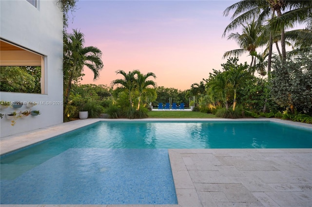 pool at dusk with an outdoor pool and a patio