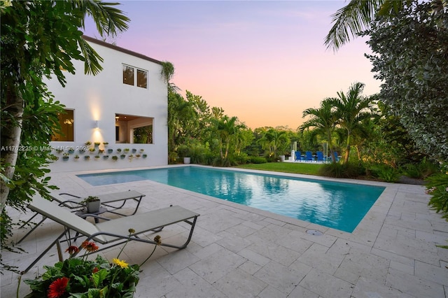 pool at dusk featuring an outdoor pool and a patio area