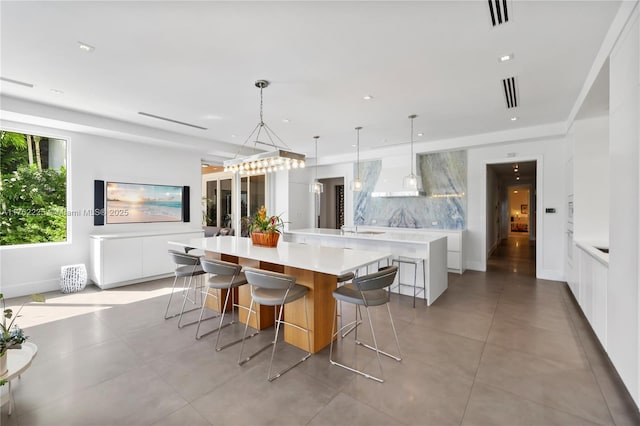 kitchen with visible vents, a large island with sink, light countertops, modern cabinets, and backsplash