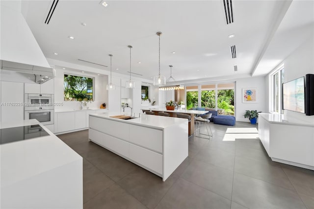 kitchen with a spacious island, custom exhaust hood, modern cabinets, black electric cooktop, and a sink