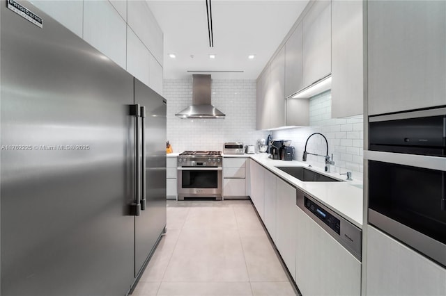 kitchen with a sink, wall chimney exhaust hood, light tile patterned floors, decorative backsplash, and high end appliances