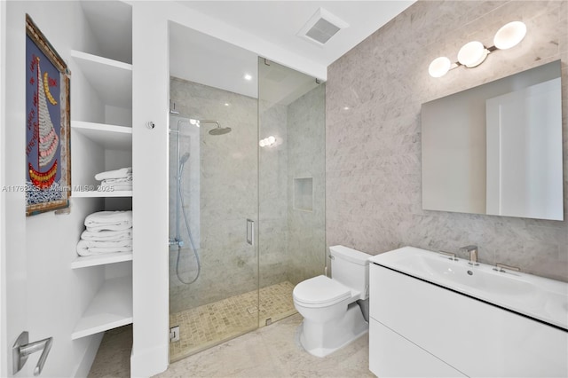 bathroom featuring visible vents, toilet, vanity, a stall shower, and tile walls