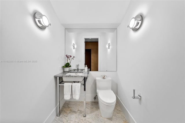 half bath with marble finish floor, toilet, baseboards, and a sink