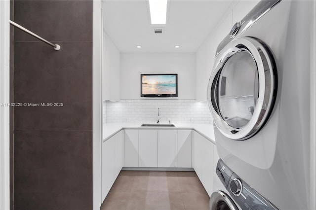 washroom featuring light tile patterned floors, visible vents, stacked washing maching and dryer, cabinet space, and a sink